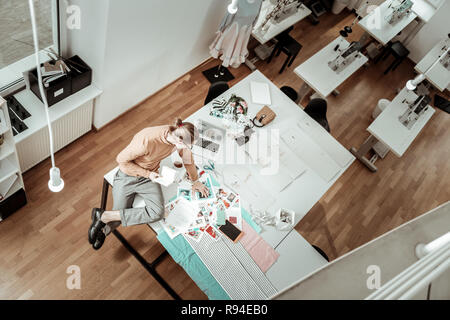 Long-haired tall designer in a brown garment working on new models sketches Stock Photo