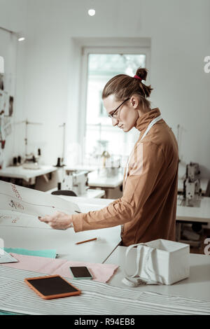 Long-haired handsome designer in a brown garment working on a curve Stock Photo