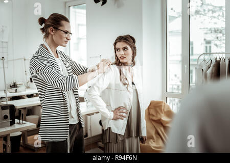 Pretty dark-haired model with wide eyebrows trying on a new jacket Stock Photo