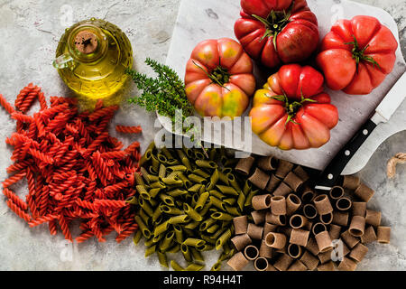 multicolor gluten-free pasta with ingredients from which it is made on a stone table with brandywine tomato and olive oil Stock Photo