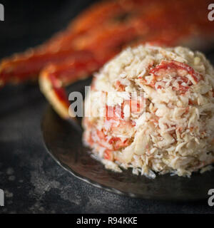 Luxury crab meat for salad at black plate with crab claw on black background. Holiday dish. Menu Stock Photo