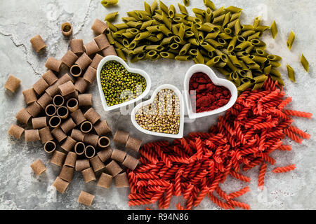 multicolor gluten-free pasta with ingredients in bowls in the form of hearts from which it is made on a stone table Stock Photo