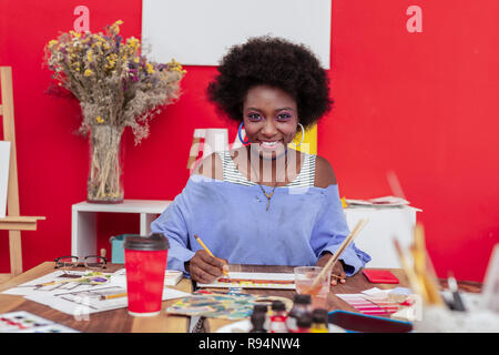 Cheerful designer wearing massive earrings smiling broadly Stock Photo