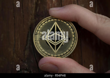 Ethereum Classic cryptocurrency physical coin held in between the fingers against the wooden background Stock Photo