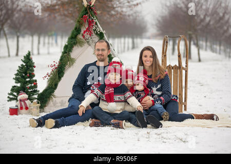 Happy family with kids, having fun outdoor in the snow on Christmas, playing with sledge, teepee and christmas decoration Stock Photo
