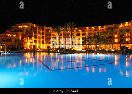 Pool and evening hotel on vacation. People relax by evening near pool. Lights of evening hotel are reflected in pool water in night. Bright lights of  Stock Photo
