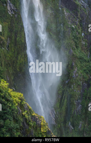 Detail of a portion of Stirling Falls with misty water falling down a green moss-covered rock cliff into Milford Sound in Fiordland National Park on t Stock Photo