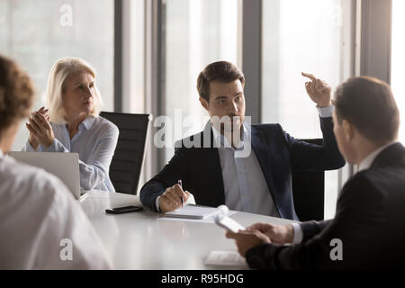 Serious businesspeople discussing new project sitting at desk in Stock Photo