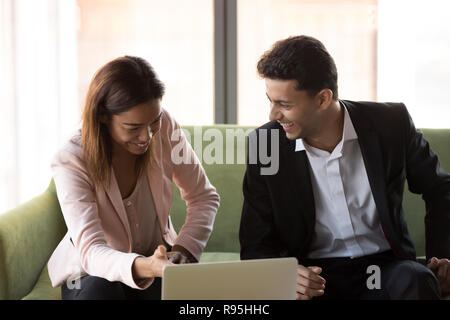 Funny diverse colleagues using laptop sitting on couch at work Stock Photo