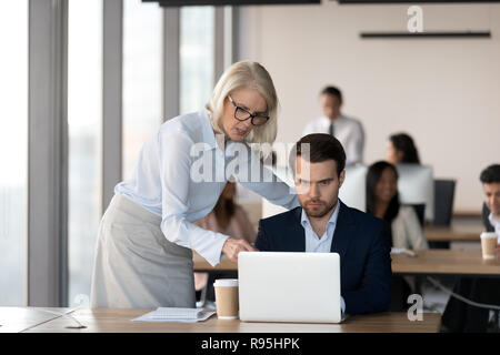 Middle aged executive manager helping to male colleague Stock Photo