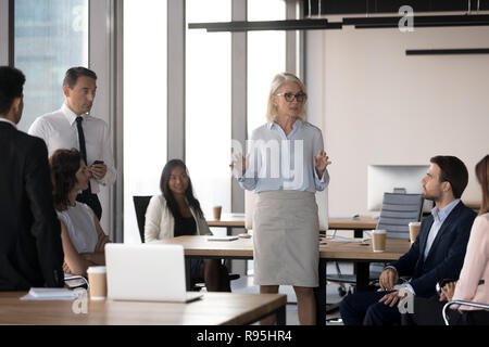 Middle aged attractive serious coach talking with company staff Stock Photo