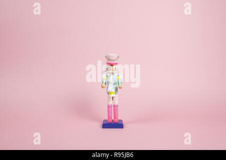 wood nutcracker figurine placed on a pink background. Color harmony. Minimal still life color photography Stock Photo