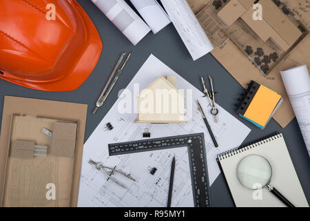 Workplace of architect - note pad, construction drawings and engineering tools, little house, magnifying glass, helmet on grey background Stock Photo