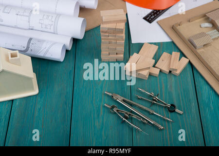 Workplace of architect - construction drawings and engineering tools, little house, model house from wooden blocks on blue wooden background Stock Photo