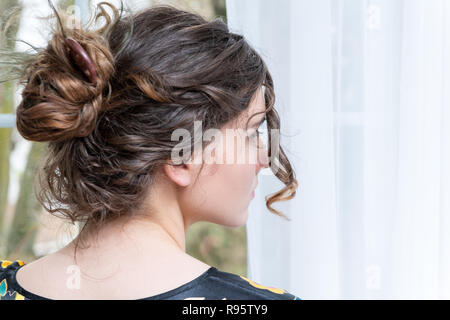 Closeup portrait of female caucasian person back, young woman standing, dressed in Asian, Chinese traditional robe dress by window, white curtains, bu Stock Photo