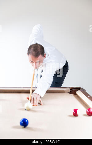 Young man, businessman in tie, white shirt, pants holding cue by pool table, playing game of snooker, billiard, billiards, striking white ball, many c Stock Photo