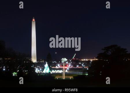 View of the Washington Monument and National Mall from the South Lawn of the White House decorated for Christmas and lighted at night December 12, 2018 in Washington, DC. The light streaks are commercial airplanes taking off from Reagan National Airport on the Potomac River. Stock Photo