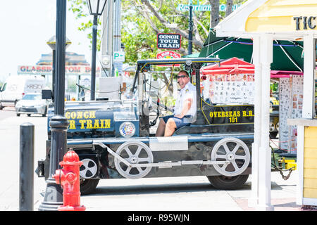 Key West, USA - May 1, 2018: Male person, man, driver driving, riding yellow color tour bus trolley with tourists at street road in Florida island on  Stock Photo