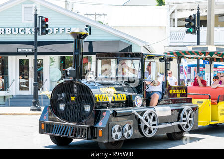 Key West, USA - May 1, 2018: People, tourists riding yellow color old town bus trolley at street road in Florida island on travel, sunny day, Conch Tr Stock Photo