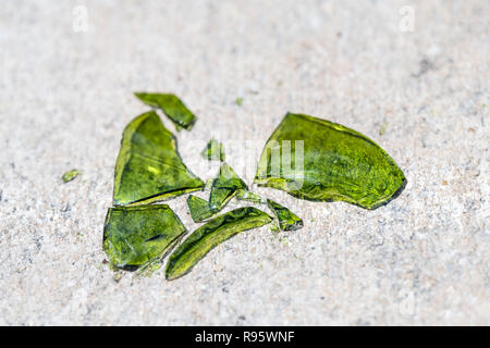 Closeup of many shattered, broken pieces, fragments, parts of green glass bottle on ground, sidewalk pavement, asphalt Stock Photo