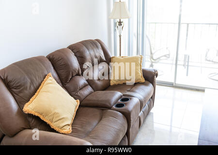 Brown leather couch with cushions, lamp, table with bright natural light, balcony in background in house, home apartment living room, tiles, tiled flo Stock Photo