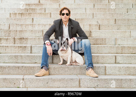 Urban scene. Man dressed in casual clothes sitting on some stairs posing next to his dog Stock Photo