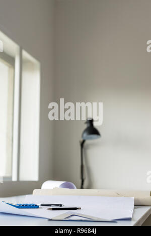 Work desk of an architect in an office with blueprints of a project , ruler, pen and calculator lying on it. Stock Photo