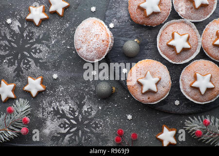 Top view of the table with sugar-sprinkled muffins and Christmas star cookies on dark textured background Stock Photo