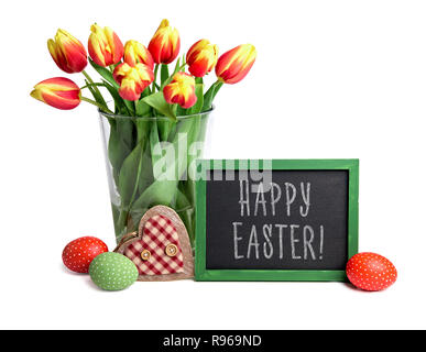 Blackboard with chalk greeting text 'Happy Easter', bunch of red stripy tulips in glass vase, Easter eggs and wooden heart isolated on white backgroun Stock Photo