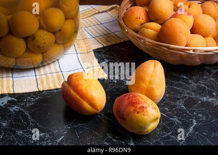 Ripe organic apricots harvested at summer time and big glass jar with canned sweet apricot compote on dark marble. Composition in rustic style - organ Stock Photo