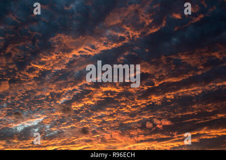 Overcast orange and grey sky right after the sun had set behind the horizon. The chiselled clouds show radial arrangement. Stock Photo