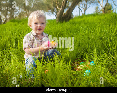 Smiling cute toddler boy holds colored eggs during Easter hunt Stock Photo