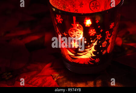 Christmas candle holder alight with a holdiay red glow, depicts scenes of winter and snow by the flame within. Stock Photo