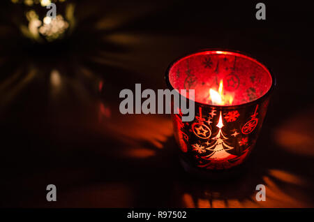 Christmas candle holder alight with a holdiay red glow, depicts scenes of winter and snow by the flame within. Stock Photo