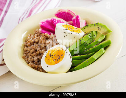 Buckwheat porridge buddha bowls with avocado, boiled eggs and  watermelon radish on white table. Healthy breakfast. Stock Photo