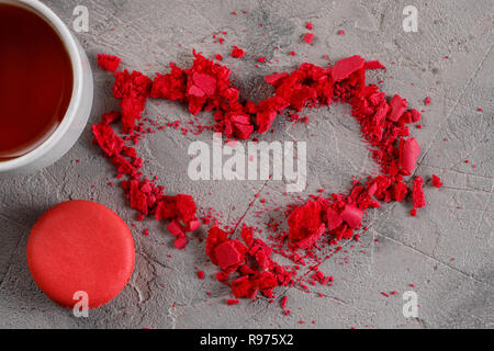 Colorful macaroons and white cup with red heart on gray background and copy space. Love concept Sweet heart from crumbs from macarons. Stock Photo