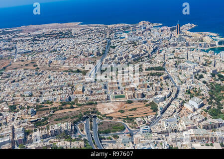 Aerial view of urban Malta. Tunnel on highway 1 under Ta' Giorni town and Paceville district, parts of St. Julian's (San Giljan) city from above. Blocks of apartment buildings, sleeping quarters. Stock Photo