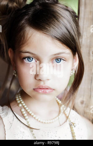 Young girl looking directly into the camera, wearing vintage pearl necklace and hair pulled back. Extreme shallow depth of field with selective focus  Stock Photo