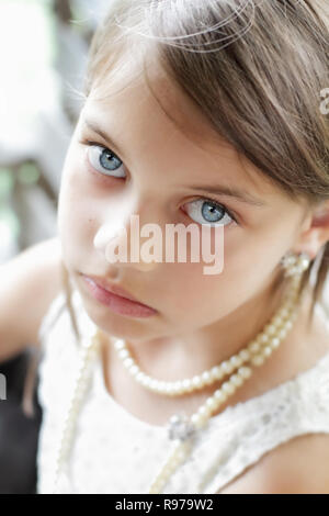 Young girl looking directly into the camera, wearing vintage pearl necklace and hair pulled back. Extreme shallow depth of field with selective focus  Stock Photo