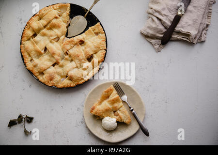 Apple pie with lattice decoration and a slice served on handmade ceramic plate with a scoop of vanilla ice-cream Stock Photo