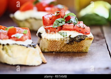 Bruschetta appetizers with tomato, mozzarella cheese, and pesto.  Blurred background with selective focus on center sandwich. Stock Photo