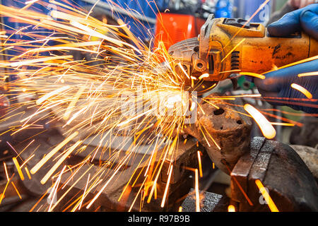 Close-up of a man sawing metal with a hand circular saw on a wooden table, bright flashes flying in different directions, in the background tools for  Stock Photo
