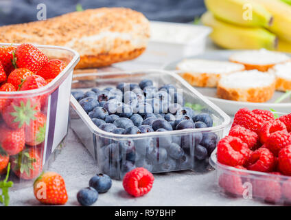 Plastic tray containers of fresh organic healthy beries and bread for fruit sandwiches. Blueberries, strawberries, bananas and raspberries on stone ki Stock Photo