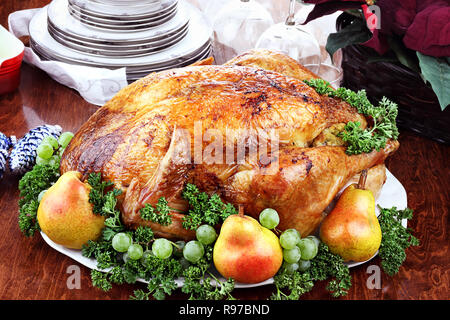 Thanksgiving or Christmas turkey dinner with fresh pears, grapes and parsley. Poinsettia flower arrangement, dishes and wine glasses in background. Stock Photo