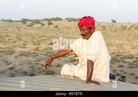 Local Indian man in traditional clothing sitting on a sand dune, Jaisalmer desert, Rajasthan, India Stock Photo