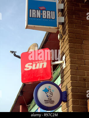 newsagent advertising sign for irn bru irn-bru , the scottish sun newspaper, the national lottery, for a shop called news and booze blue sky Stock Photo