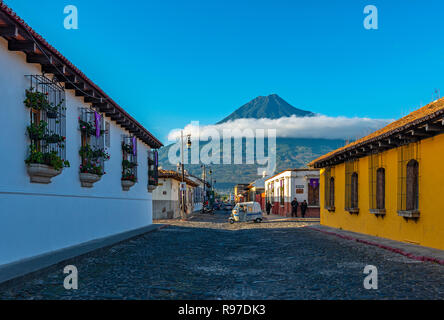 A mototaxi passing by a street crossing at sunrise in the historic city center of Antigua with the Agua volcano in the background, Guatemala. Stock Photo