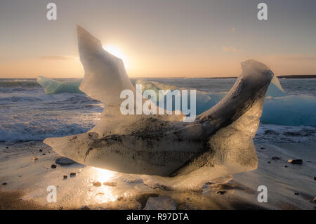 Beached block of ice on the black sand beaches of Iceland with sun setting behind Stock Photo