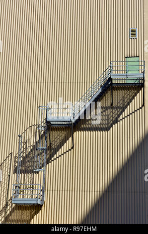 Abstract pattern of metal fire escape stairs and vertically oriented corrugated sheet metal clad building Stock Photo