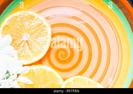 Sliced lemon and chamomile in a plate. Three cut slices of lemon lie on a multicolored plate. Stock Photo